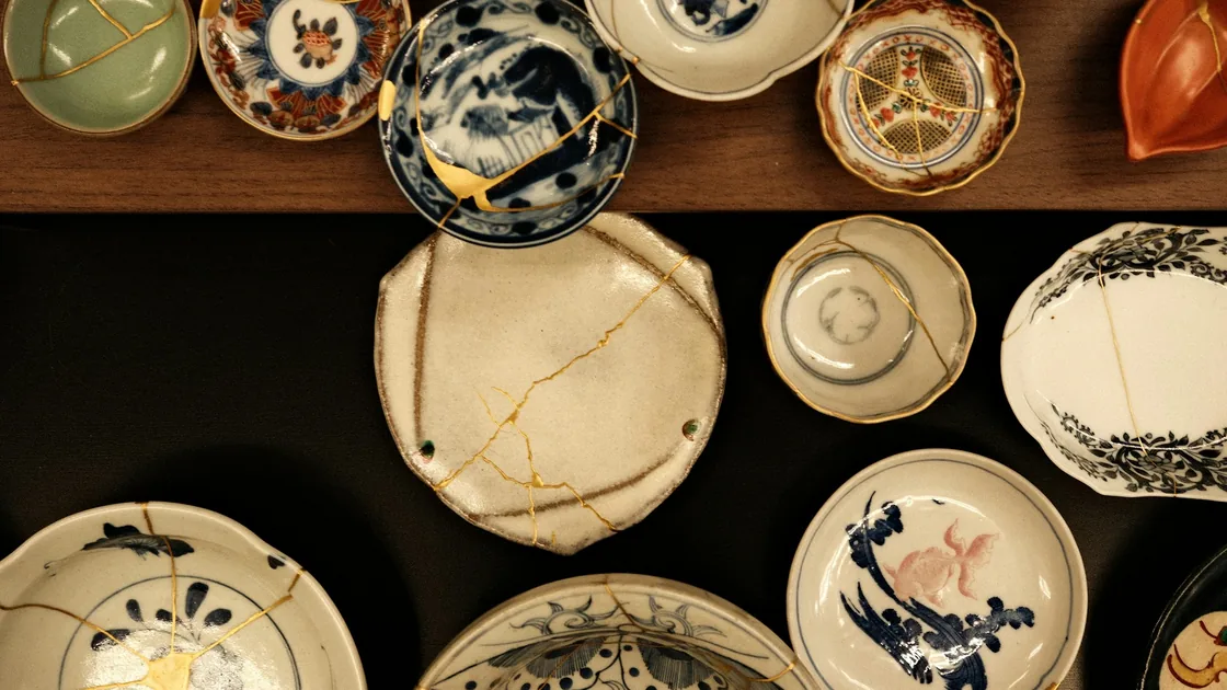 Platos y cuencos de cerámica reparados con kintsugi, con las líneas de fractura terminadas en oro, dispuestos sobre una mesa oscura